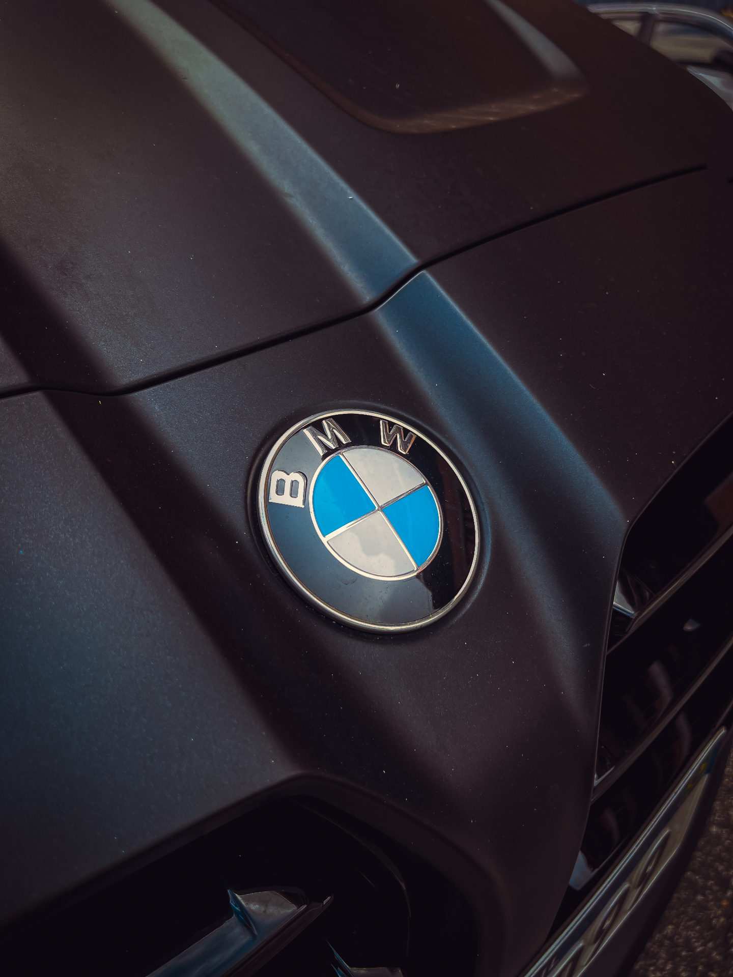 Capô fosco preto de um BMW com o emblema circular azul e branco em diagonal