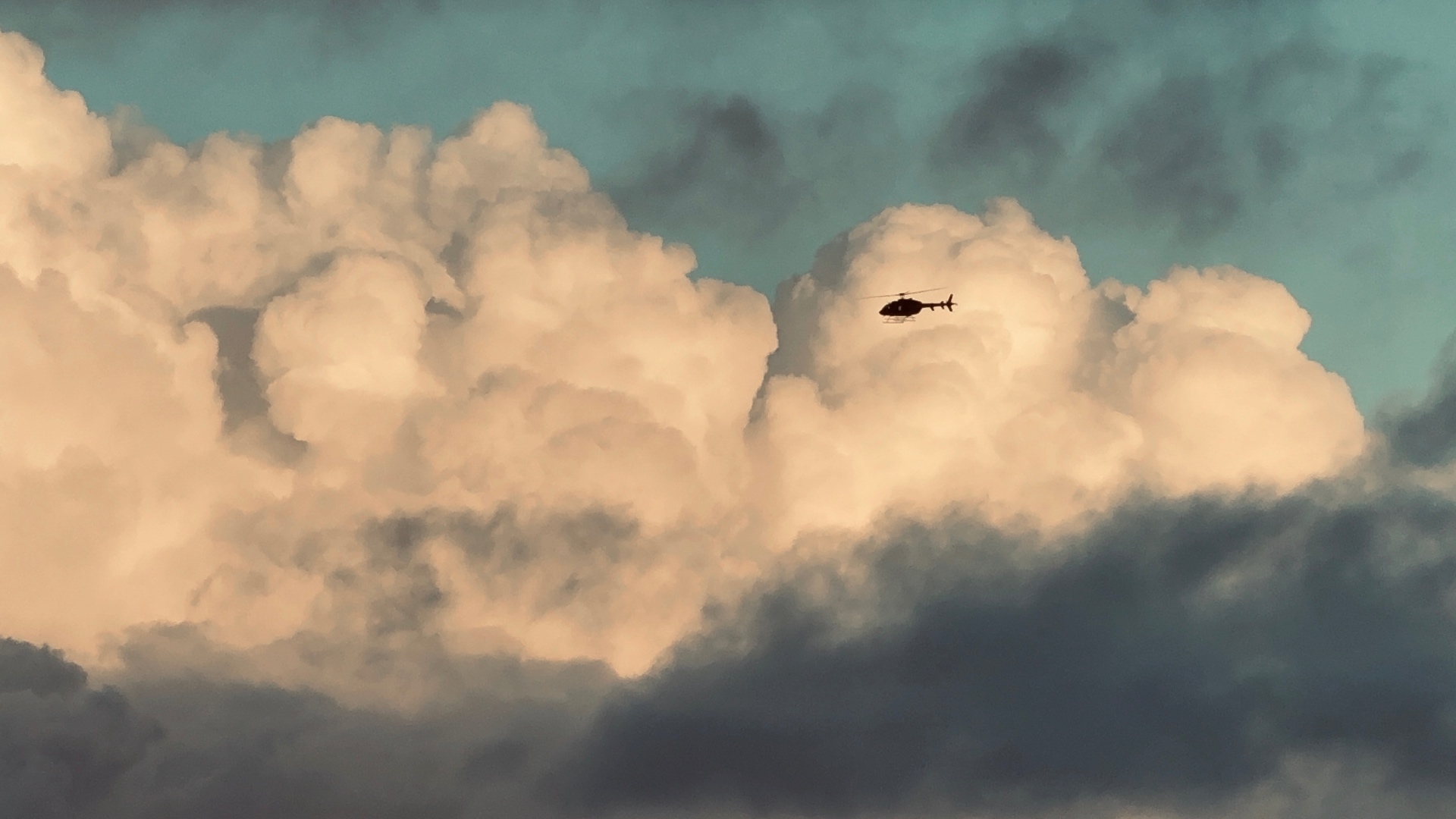 Helicóptero em silhueta recortado contra nuvem cumulus iluminada por luz dourada