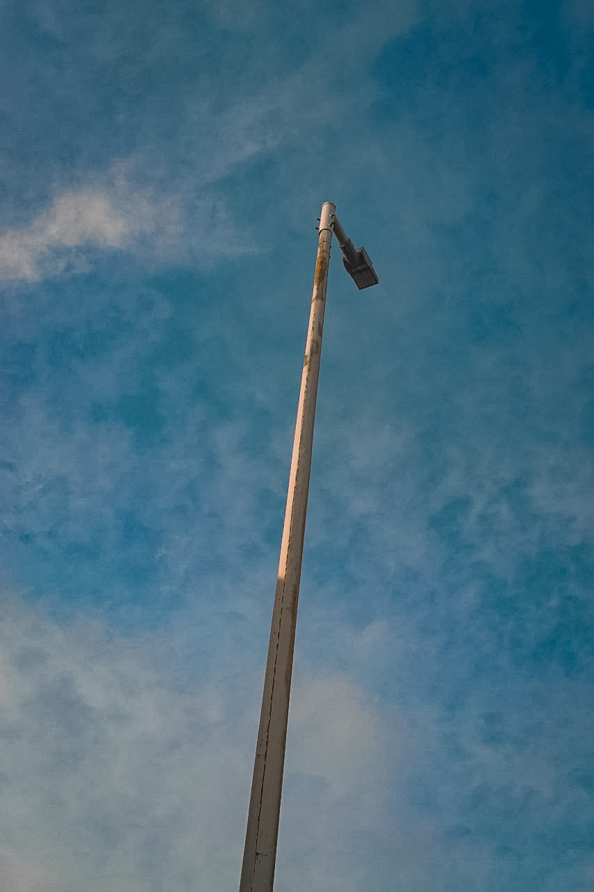 Poste de iluminação alto contra céu azul com nuvens rasgadas